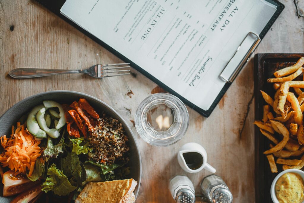 Top view of wooden table with served healthy veggie salad and french fries placed near menu and spices